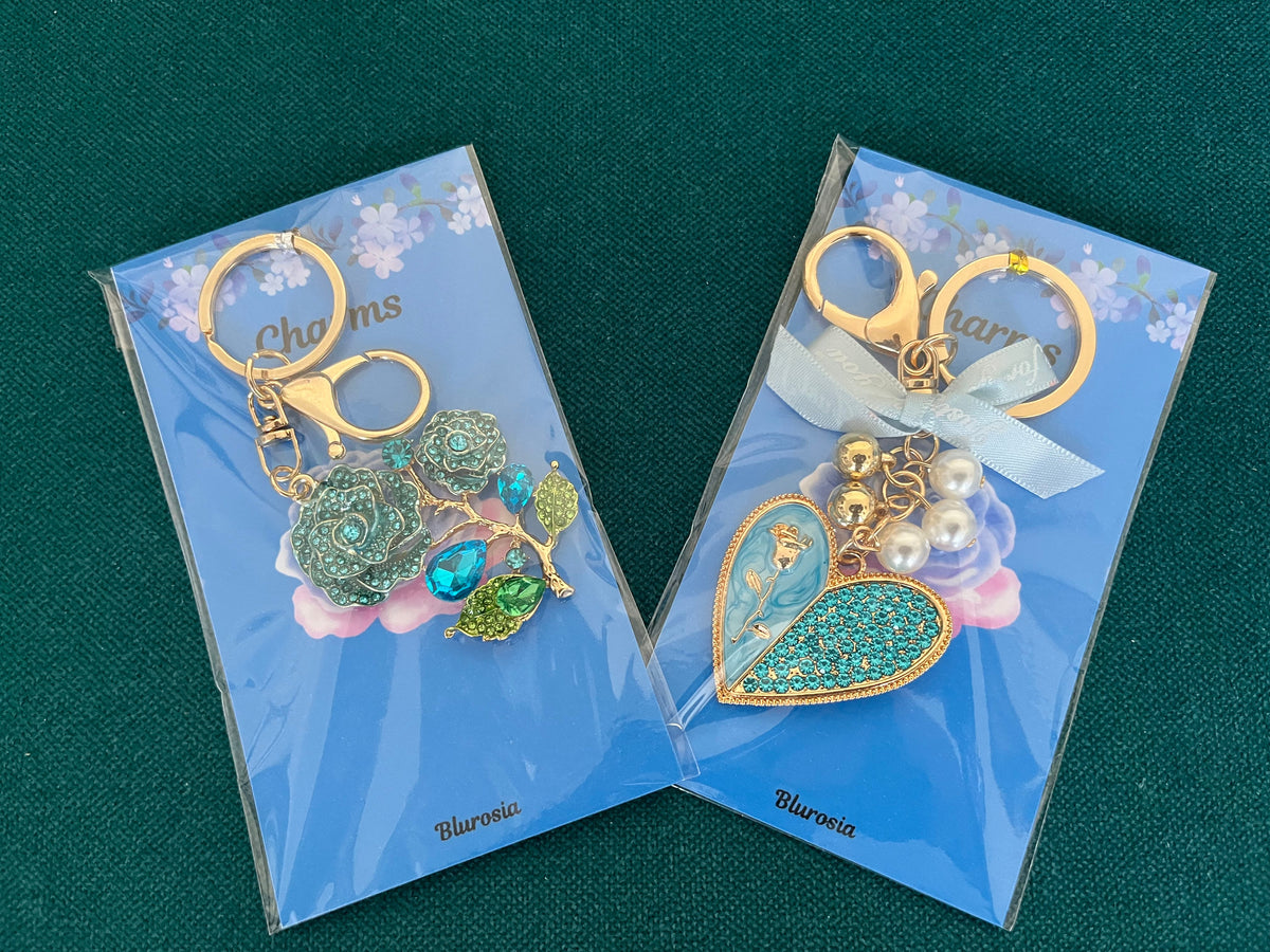 Two handmade gold-tone charm keyrings on backing cards, one with a crystal rose and one with a sparkling heart