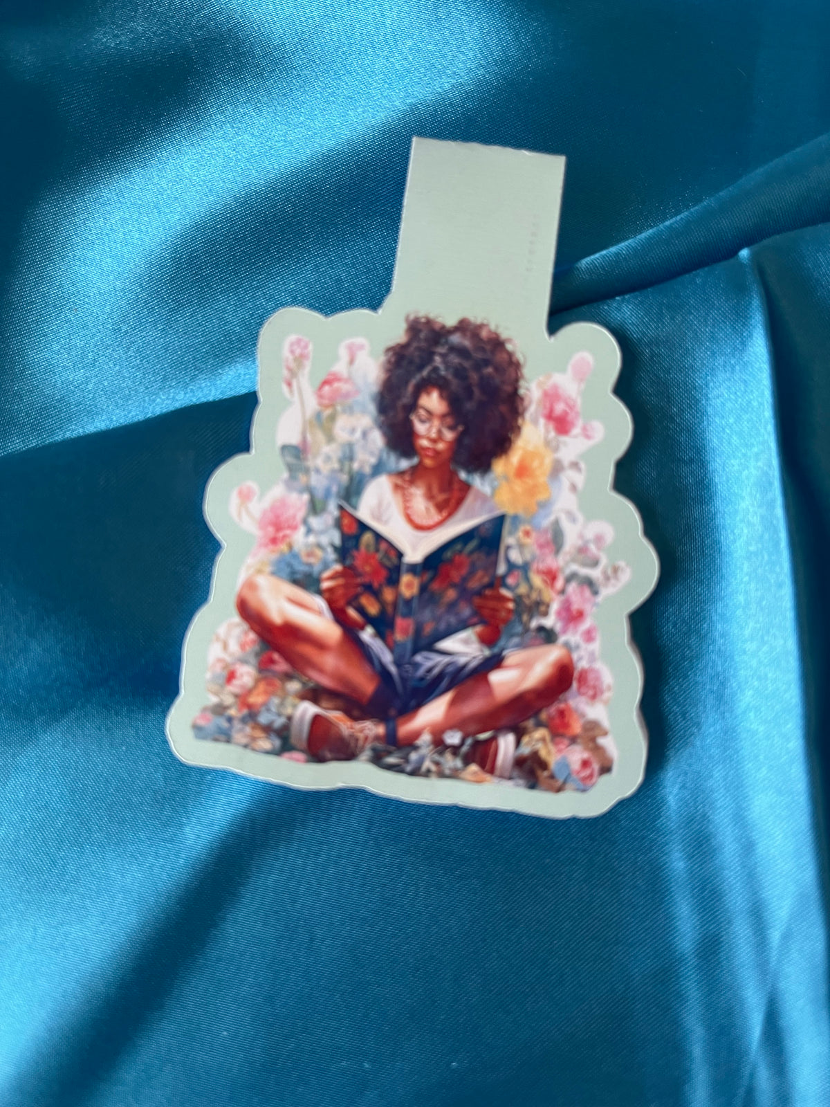 A second photograph of the handmade magnetic bookmark showing a woman reading among flowers