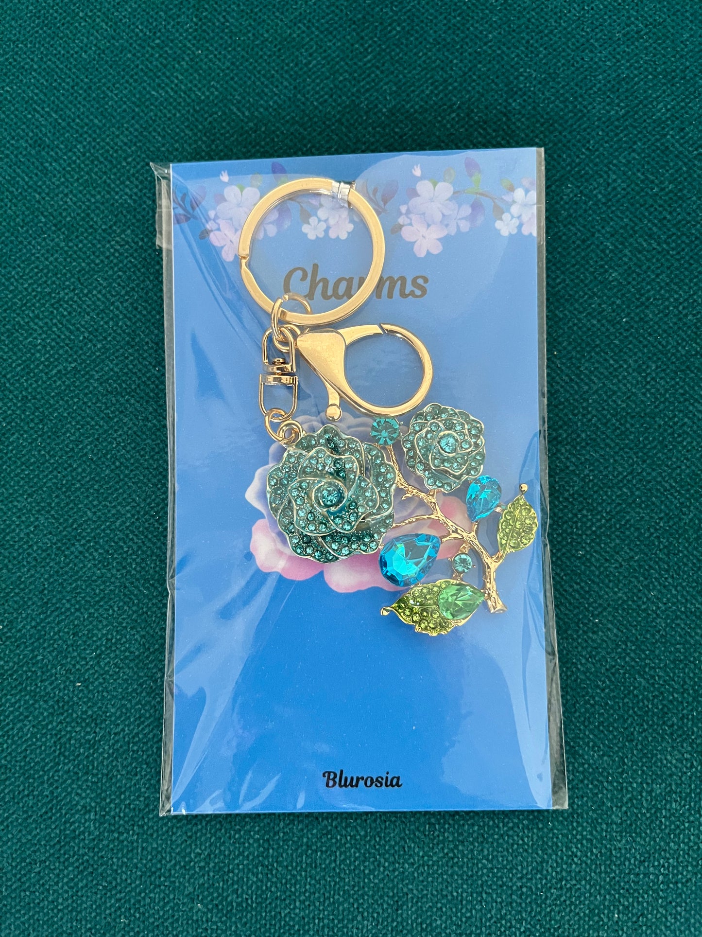 The blue rose charm keyring set with blue and green crystals, on its backing card